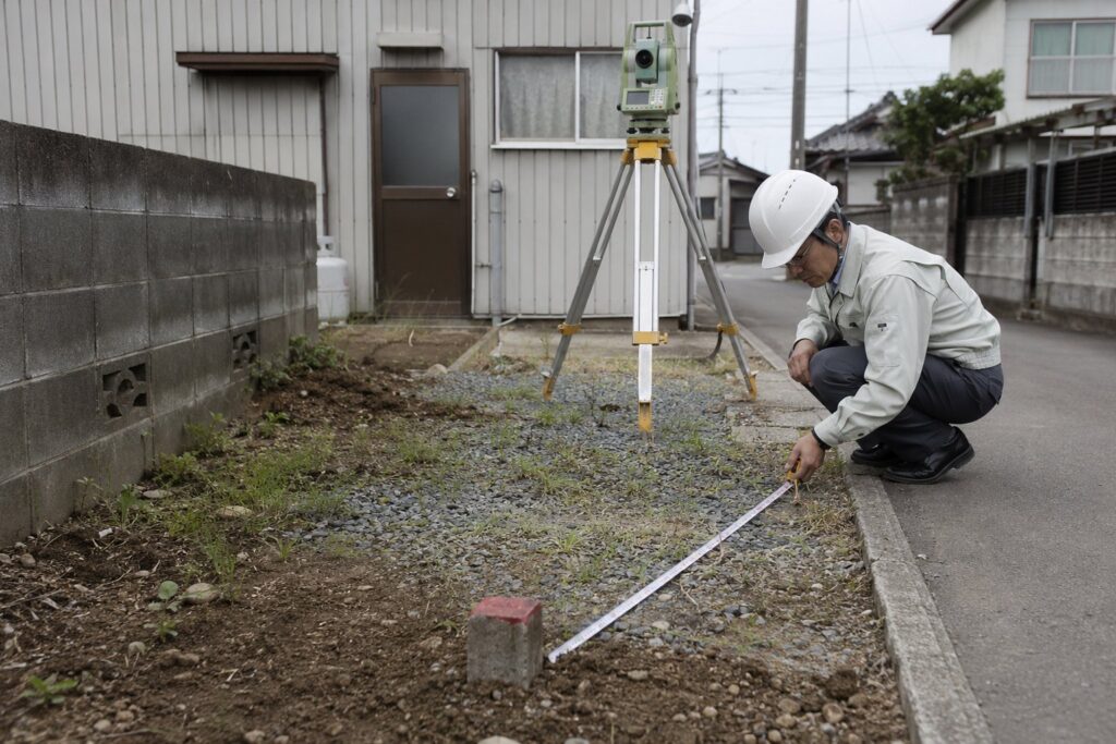 足場と養生シートに囲まれ重機で解体される木造2階建て