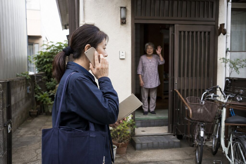 玄関先で電話をするスタッフと見送る高齢女性