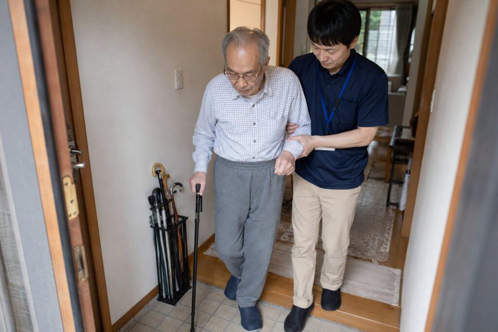 玄関の上がり框で杖をついた高齢男性を介助する様子