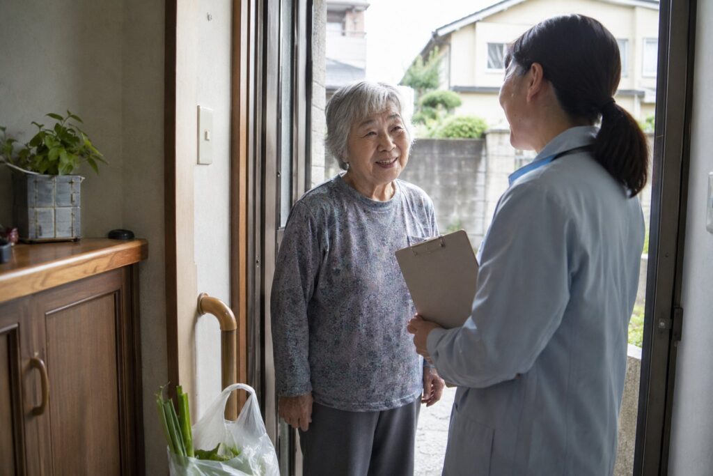 玄関先で高齢女性と話す訪問スタッフと買い物の袋