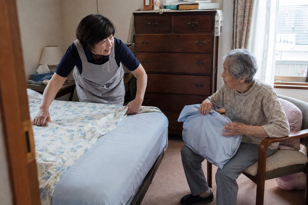 寝室でベッドの寝具を整えるスタッフと高齢の女性