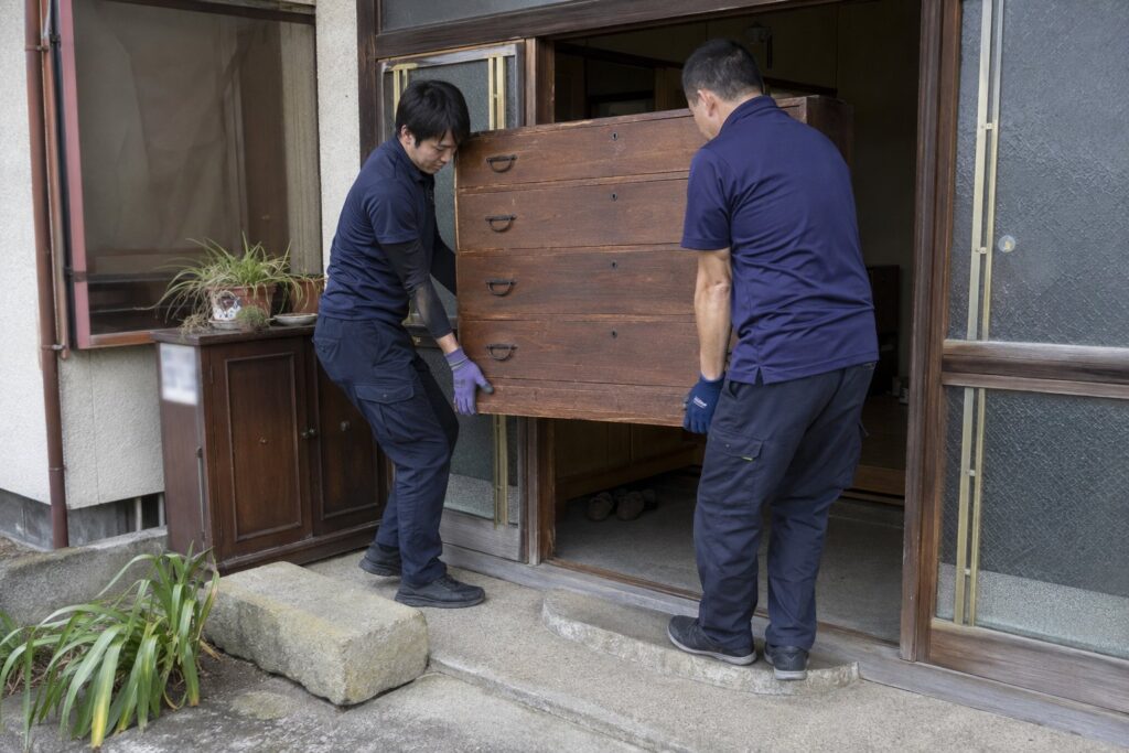 デスクトップパソコンからHDDを取り外す作業員とテレビを運び出す作業員