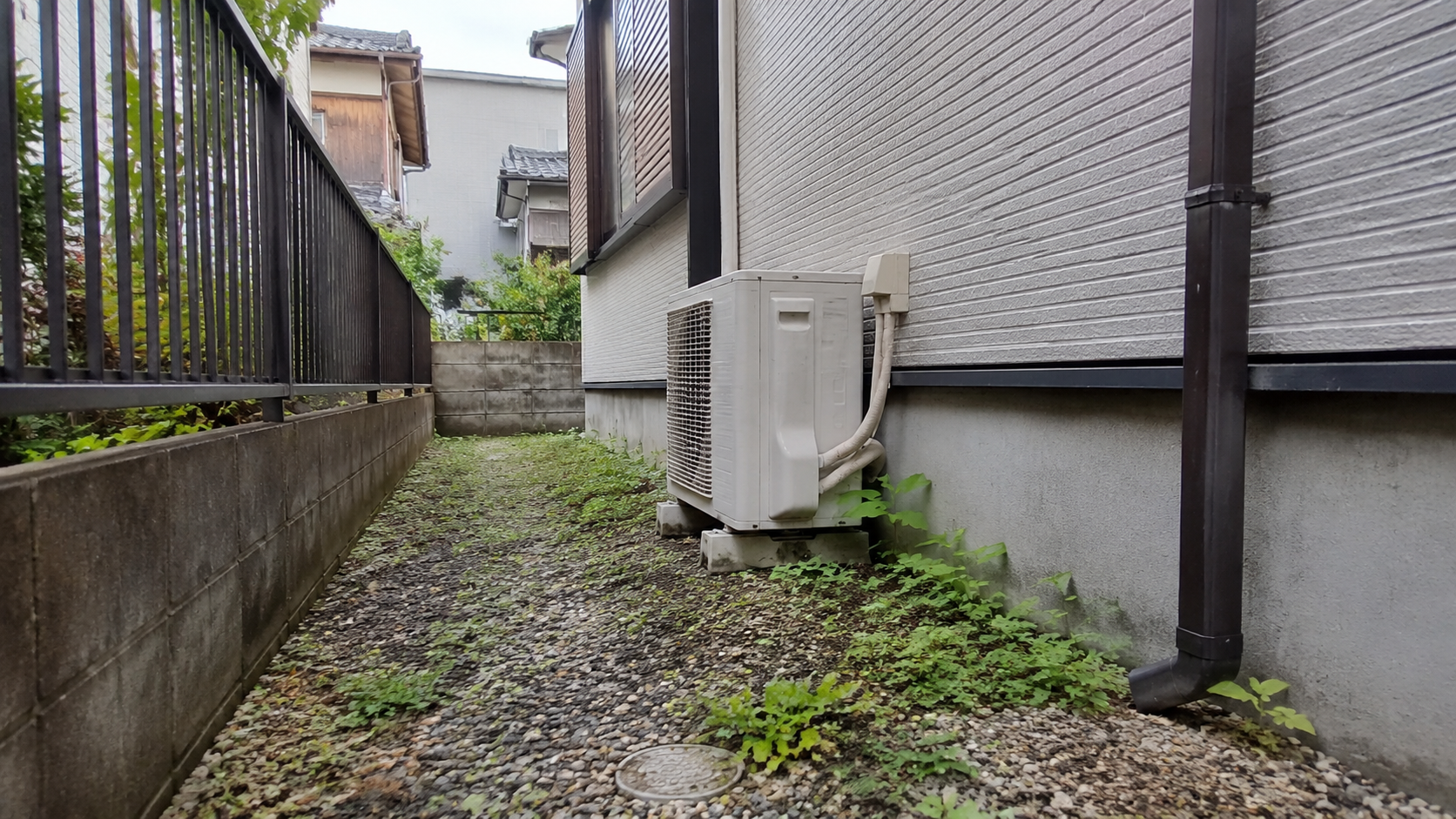 実家の建物脇にある日陰の細い通路と、エアコンの室外機